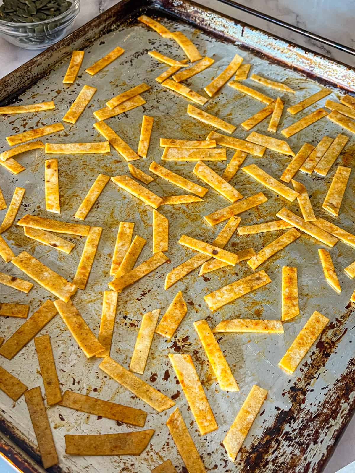 tortilla strips tossed in oil and seasoning on baking sheet.