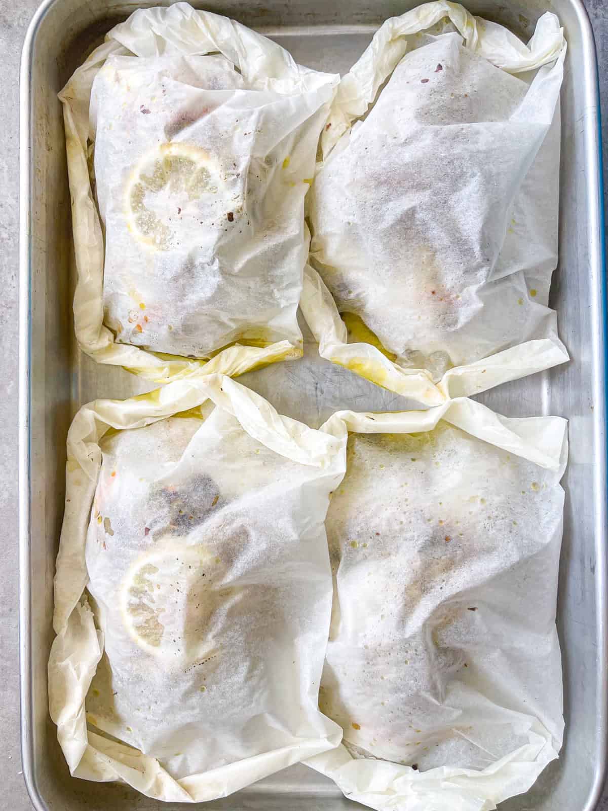 four parchment packets of grouper sealed and on a pan.