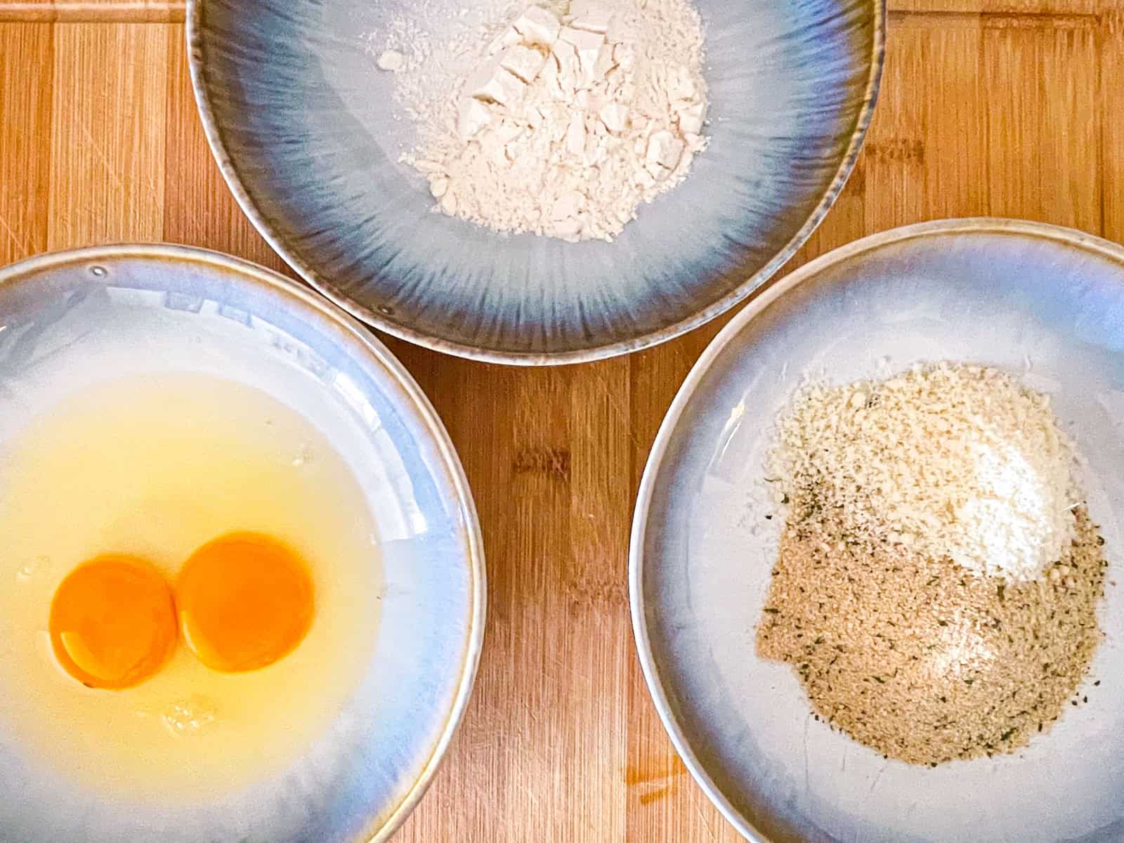 one bowl with two eggs, one with flour, one with breadcrumbs and parmesan.