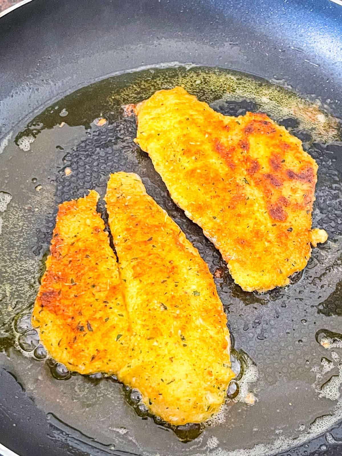 two golden, crispy fish fillets flipped in a skillet.