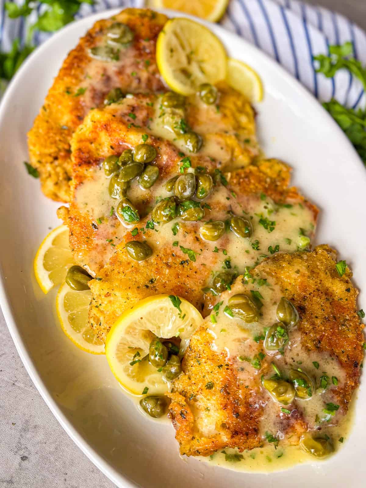 piccata sauce poured over fish fillets on a platter.