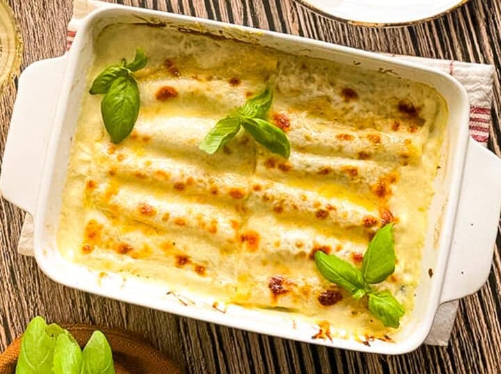 casserole dish of shrimp cannelloni in sherry cream sauce, garnished with fresh basil.