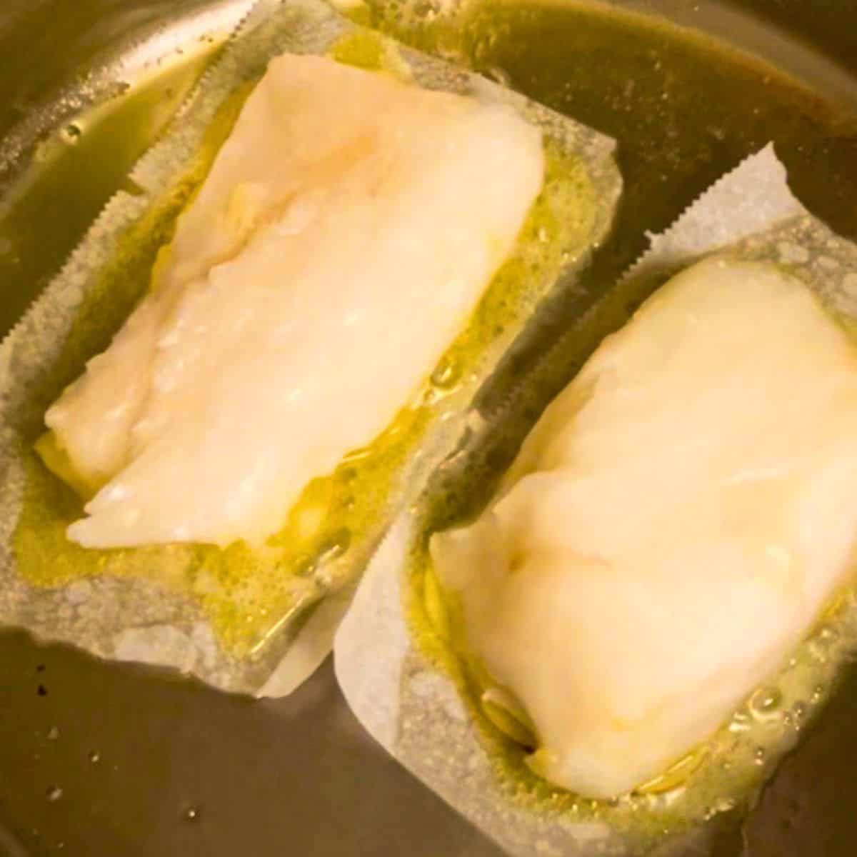 two sea bass fillets searing over parchment paper in a skillet.