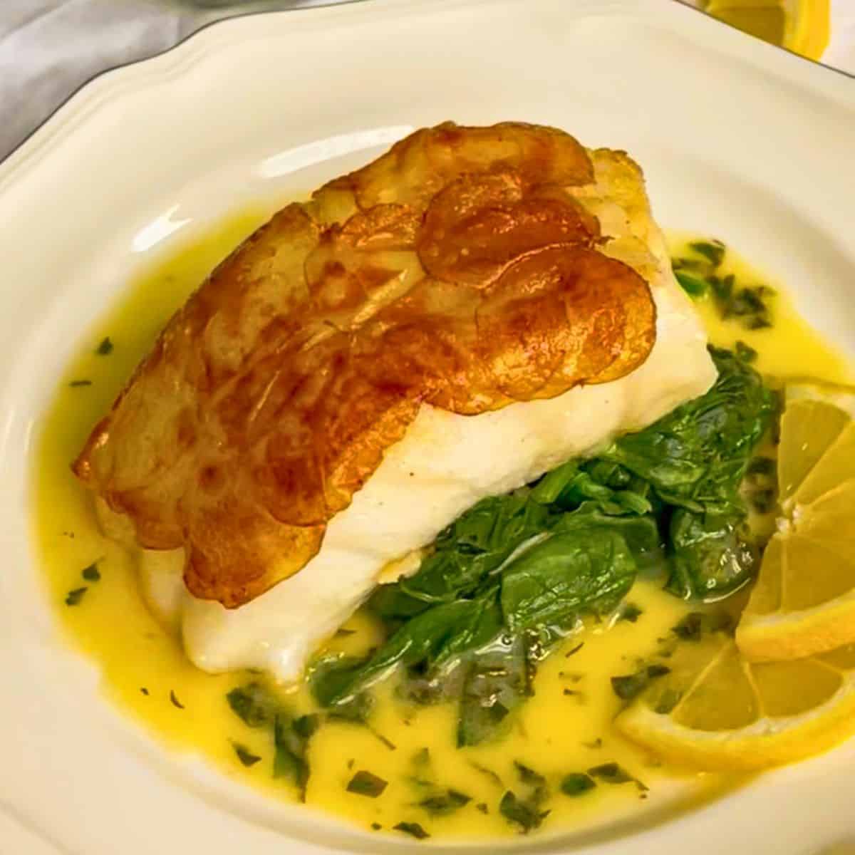 chilean sea bass fillet with crispy potato topping over lemon butter herb sauce.