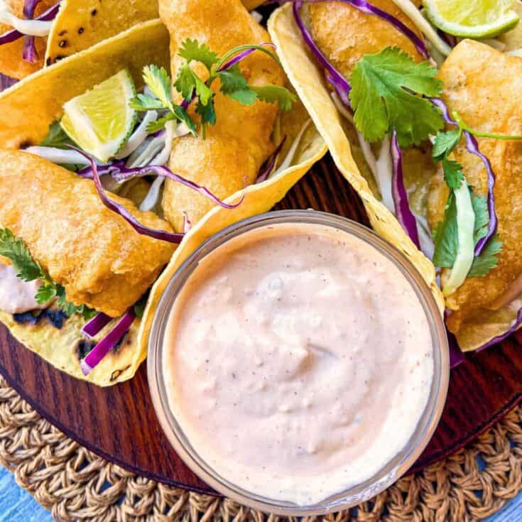 glass bowl full of creamy taco sauce on a platter of fried baja tacos