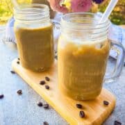 2 mason jars full of frosty iced coffee with coffee beans scattered around the table.