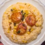 plate of three seared sea scallops in brown butter lemon sauce with basil served over polenta.