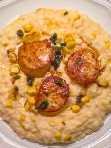 plate of three seared sea scallops in brown butter lemon sauce with basil served over polenta.