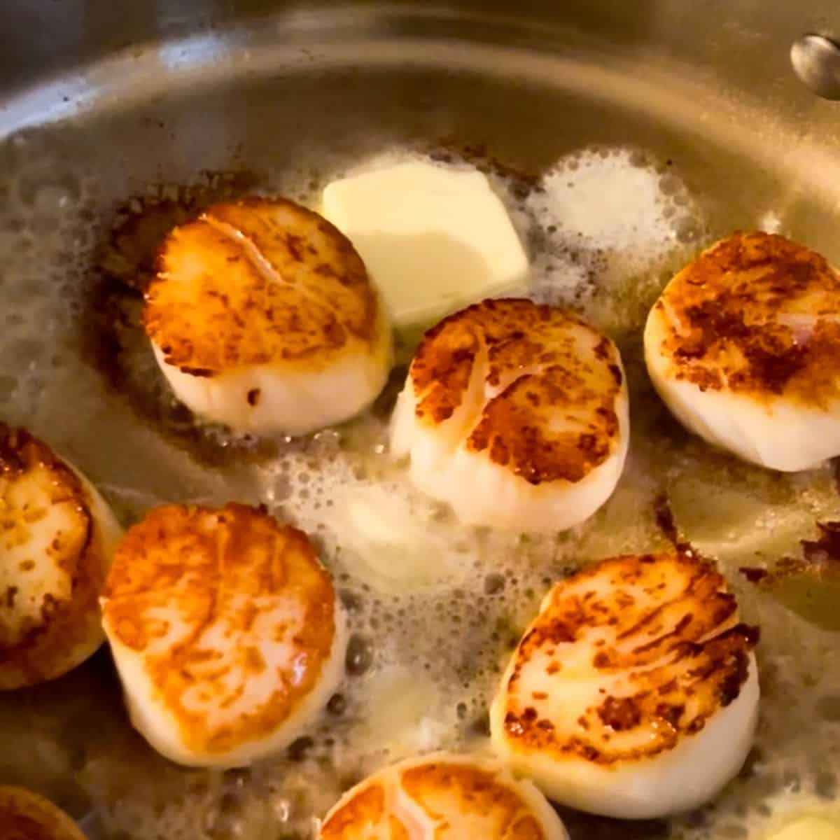 butter added to skillet of seared scallops.