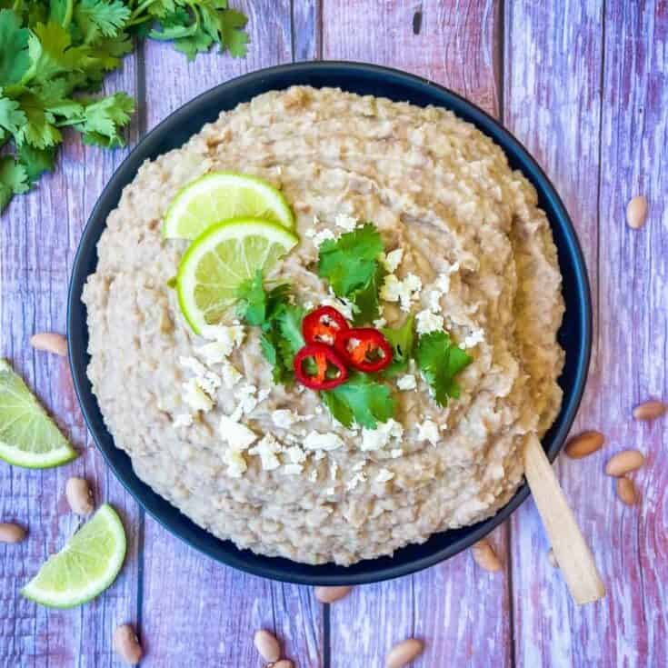 finished recipe piled high in a black plate garnished with limes, cortina cheese, cilantro and red chilis