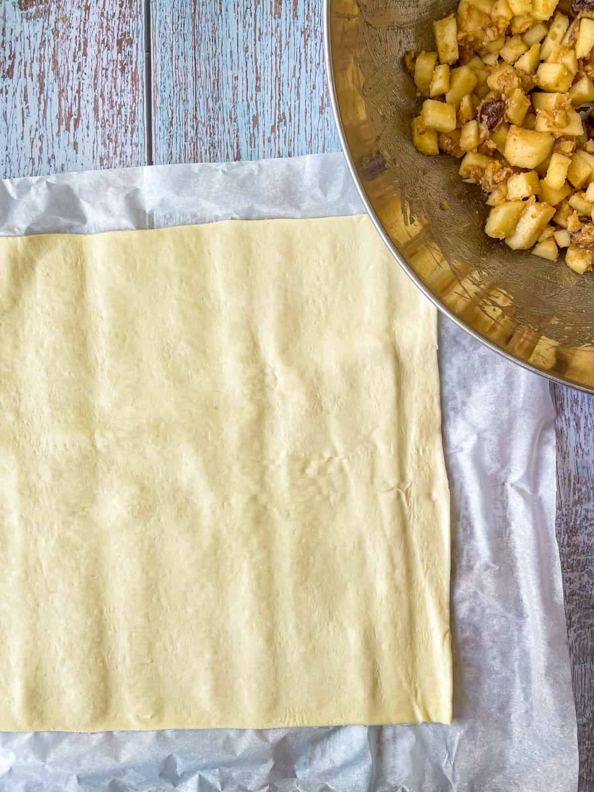 dough laid out on parchment next to bowl of apple filling