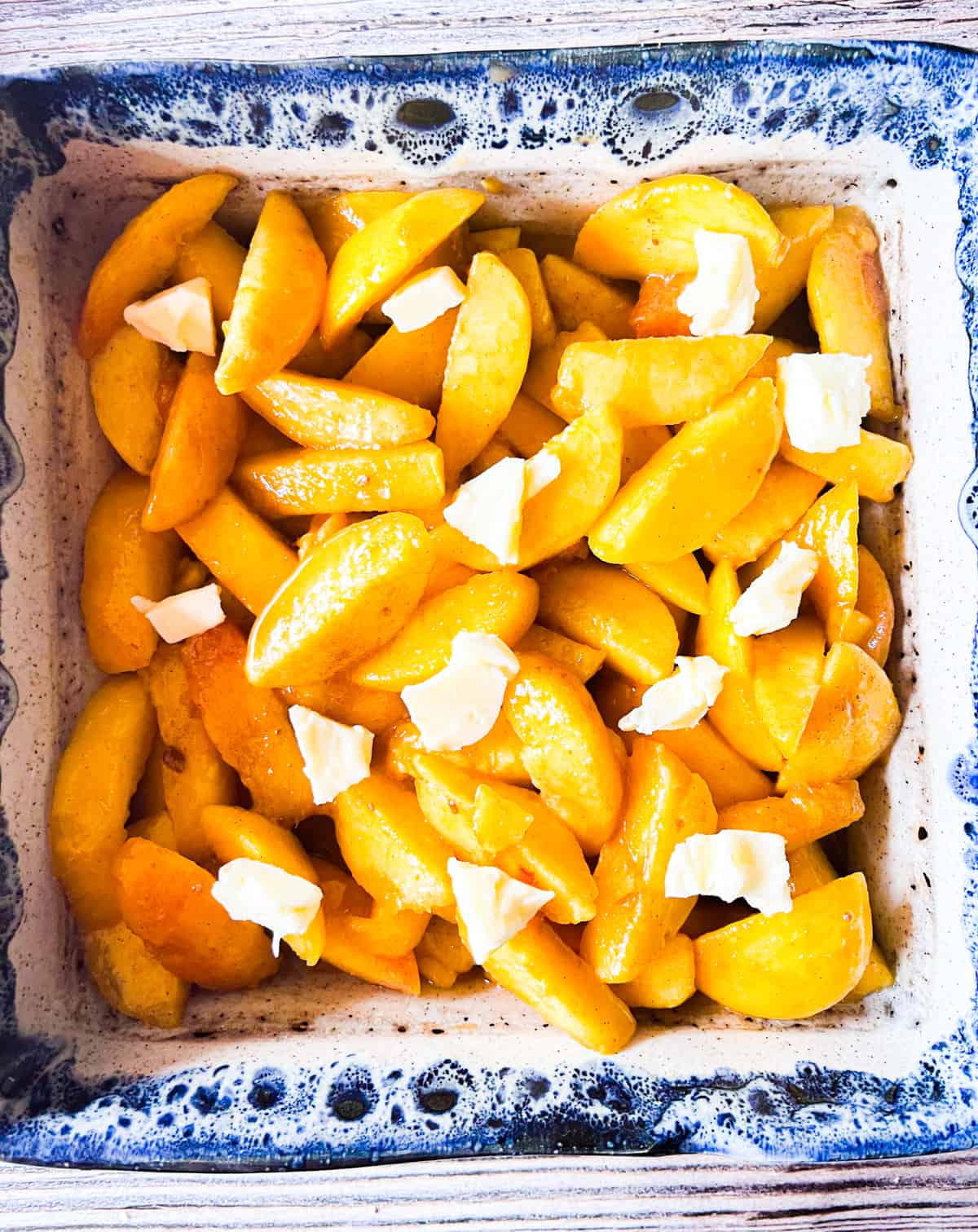 small pieces of butter layered into peach cobbler in a blue dish