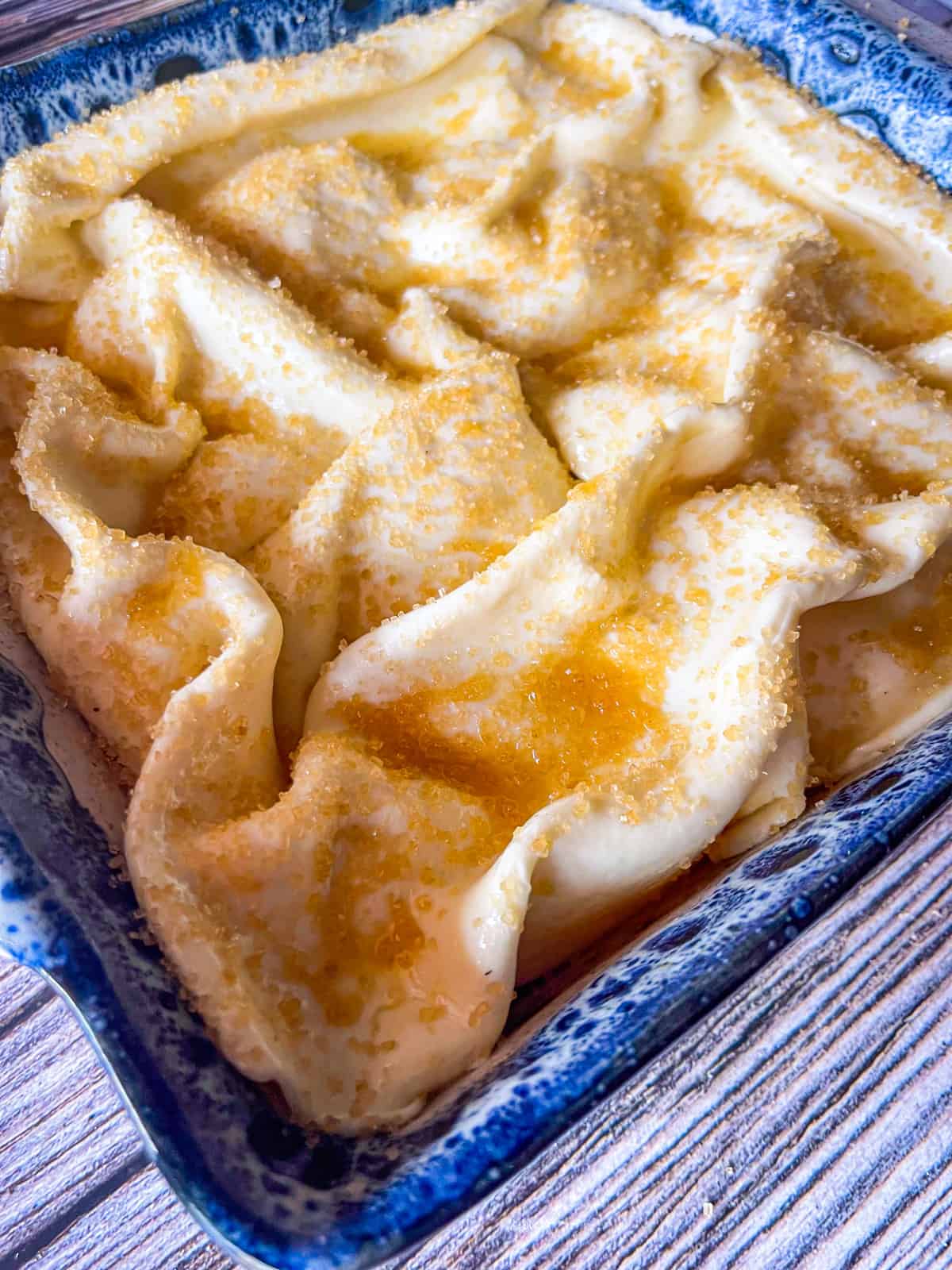 unbaked cobbler in blue dish covered with raw sugar sprinkled over crust