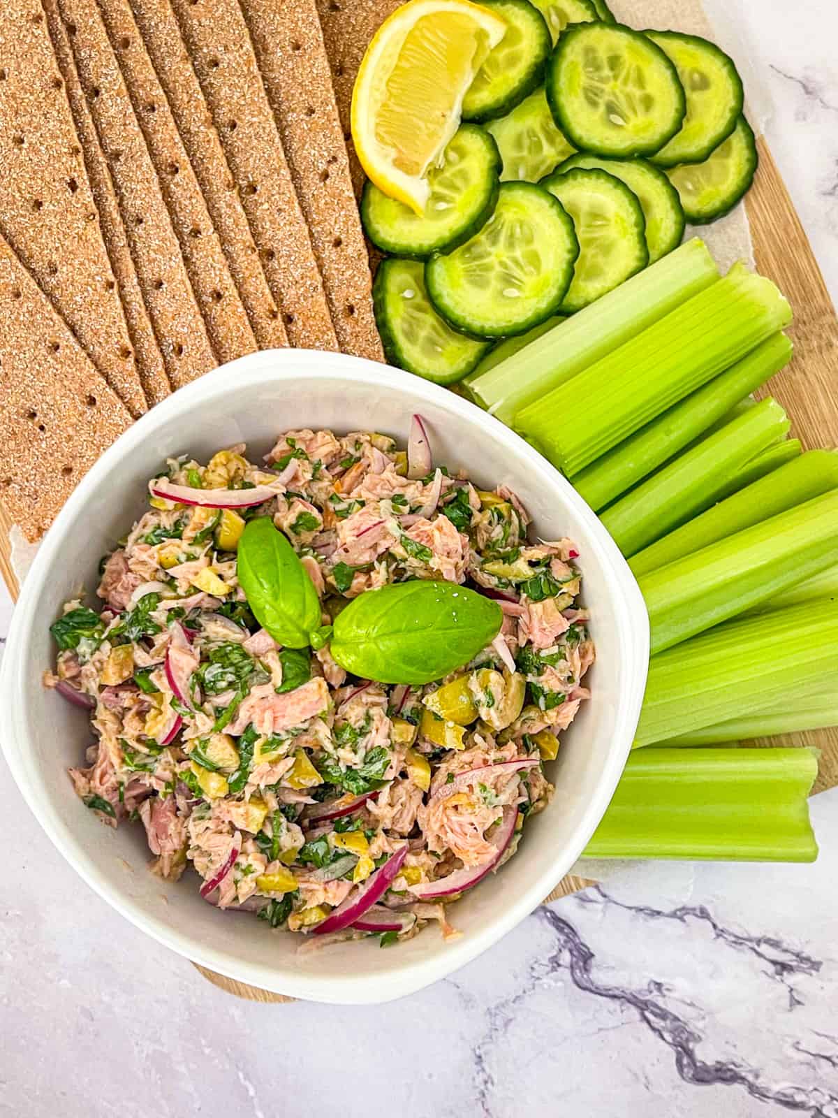 Mediterranean seafood salad in a bowl with celery sticks, sliced cucumbers and crackers
