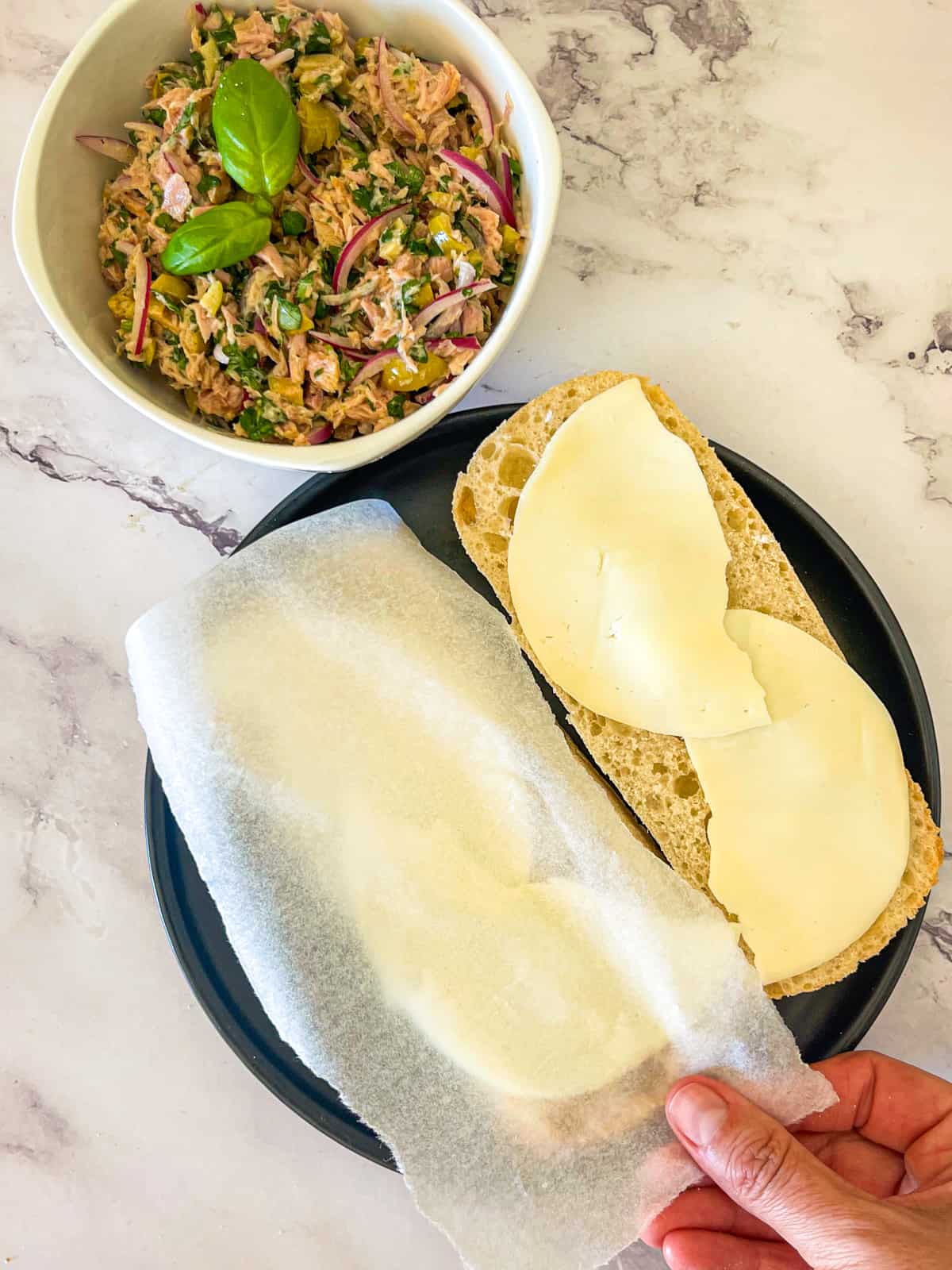 finished recipe in a bowl garnished with basil. Cheese on two slices of bread with parchment laid between them.