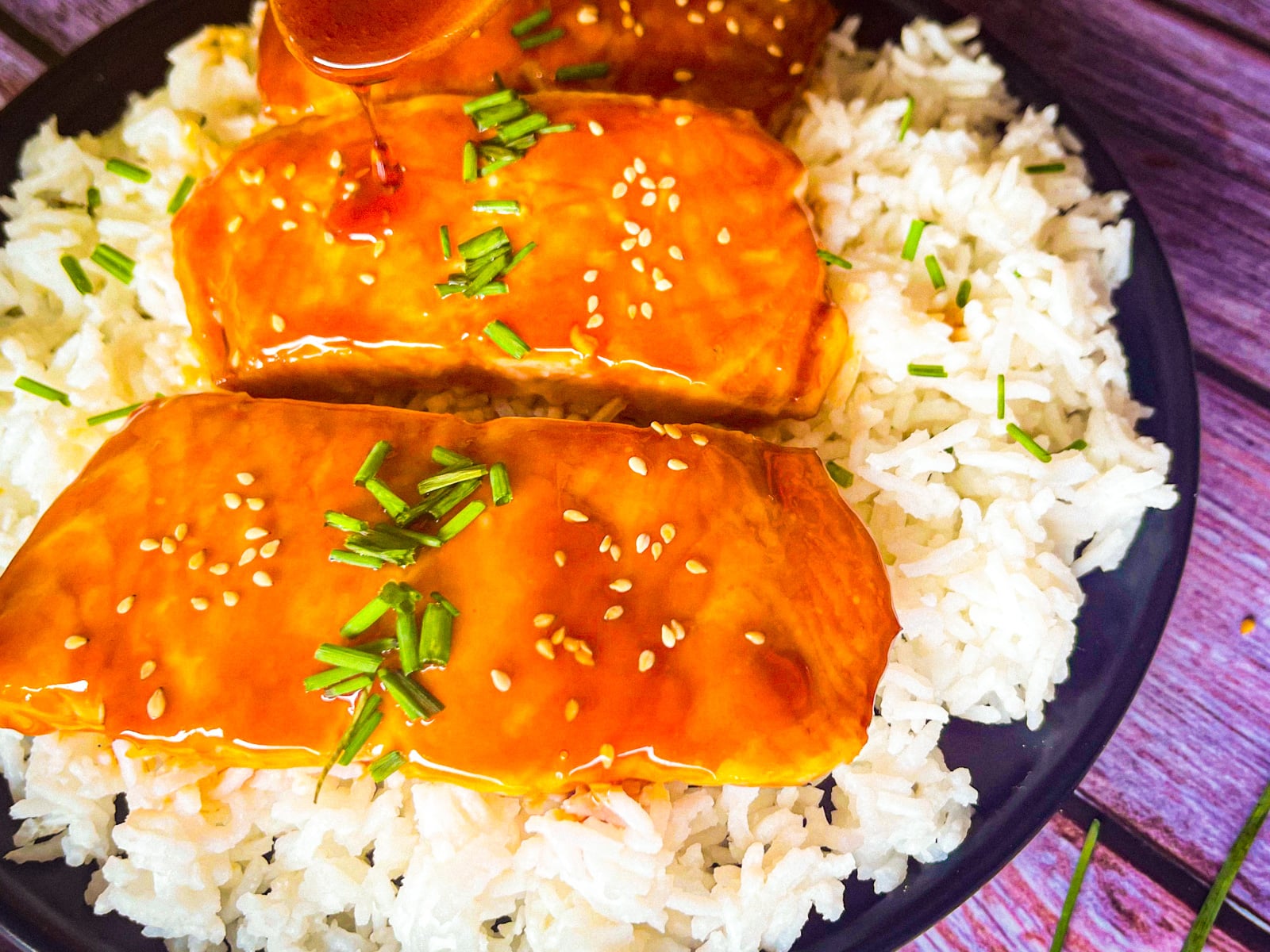 Salmon coated with sauce and garnished with diced chives and toasted sesame seeds.