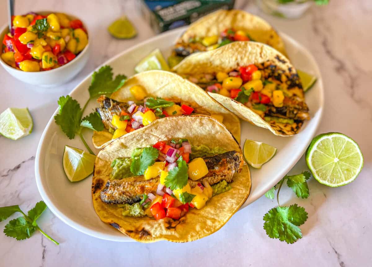 Sardine tacos with mango salsa on a white platter.
