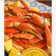 platter of snow crab legs with lemon garlic butter and lemon wedges.