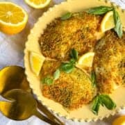 Panko Bread Crumb tilapia laid on a plate with lemons and basil.