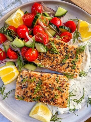2 pieces of salmon with seasoning on a bed of tzatziki and served with vegetables and garnished with dill.