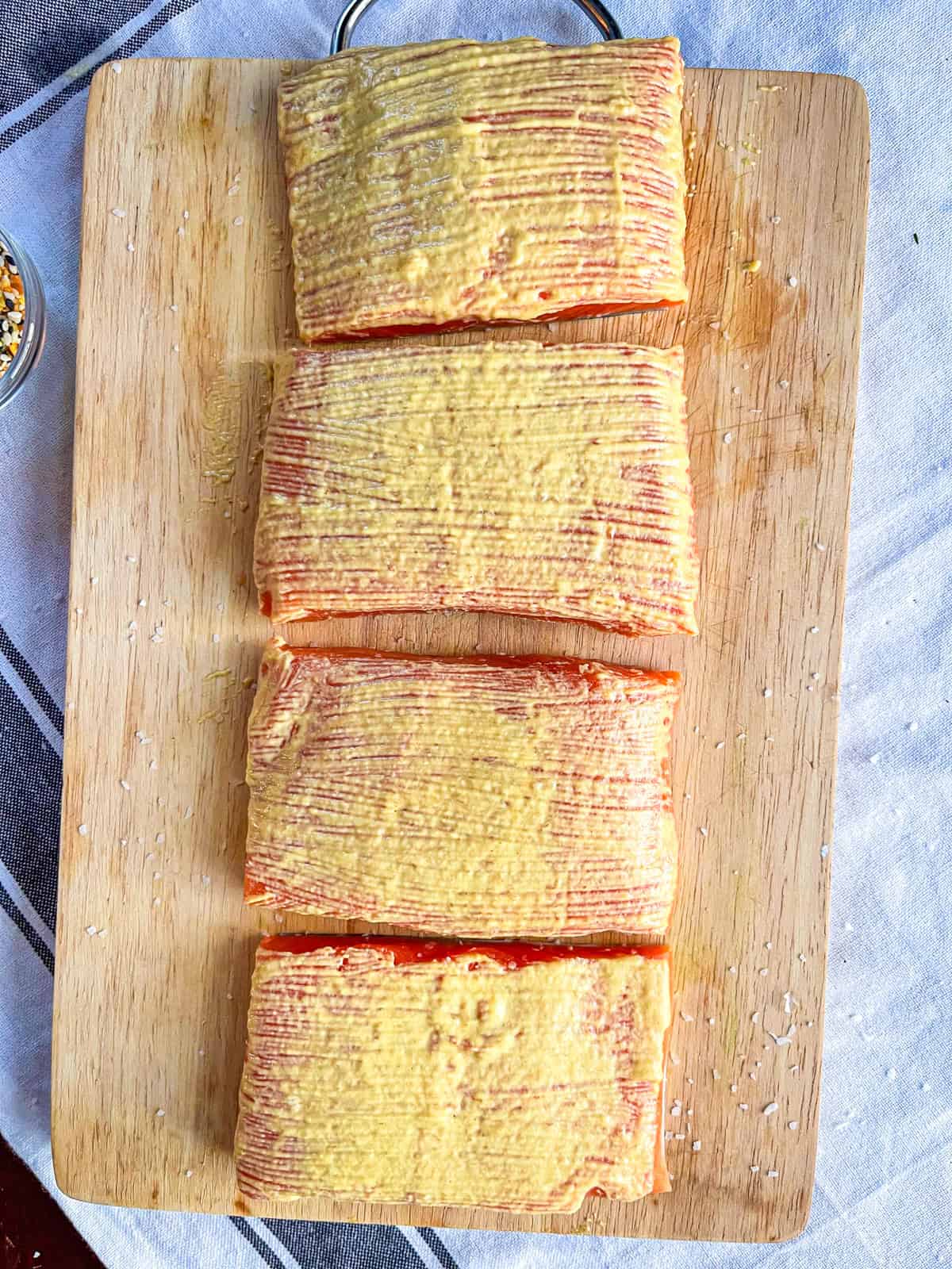 4 pieces of salmon brushed with dijon mustard on a board.
