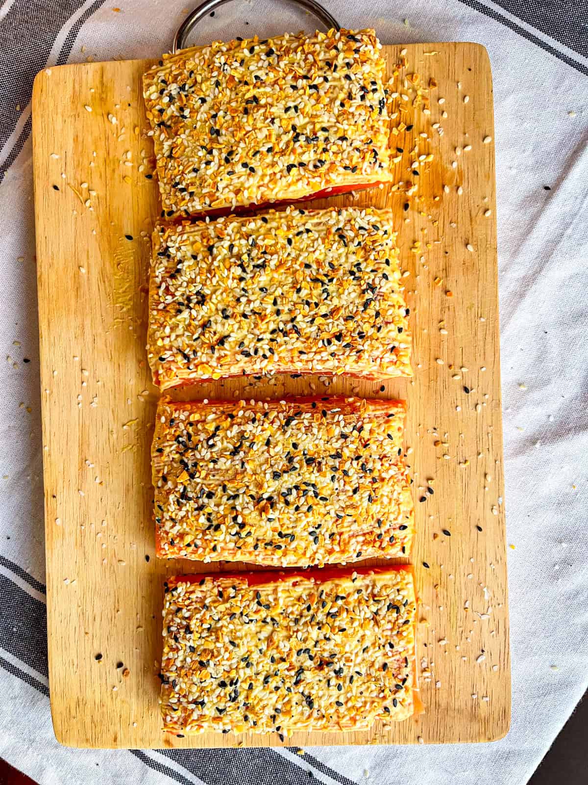 4 pieces of salmon brushed with dijon mustard and bagel seasoning on a board.