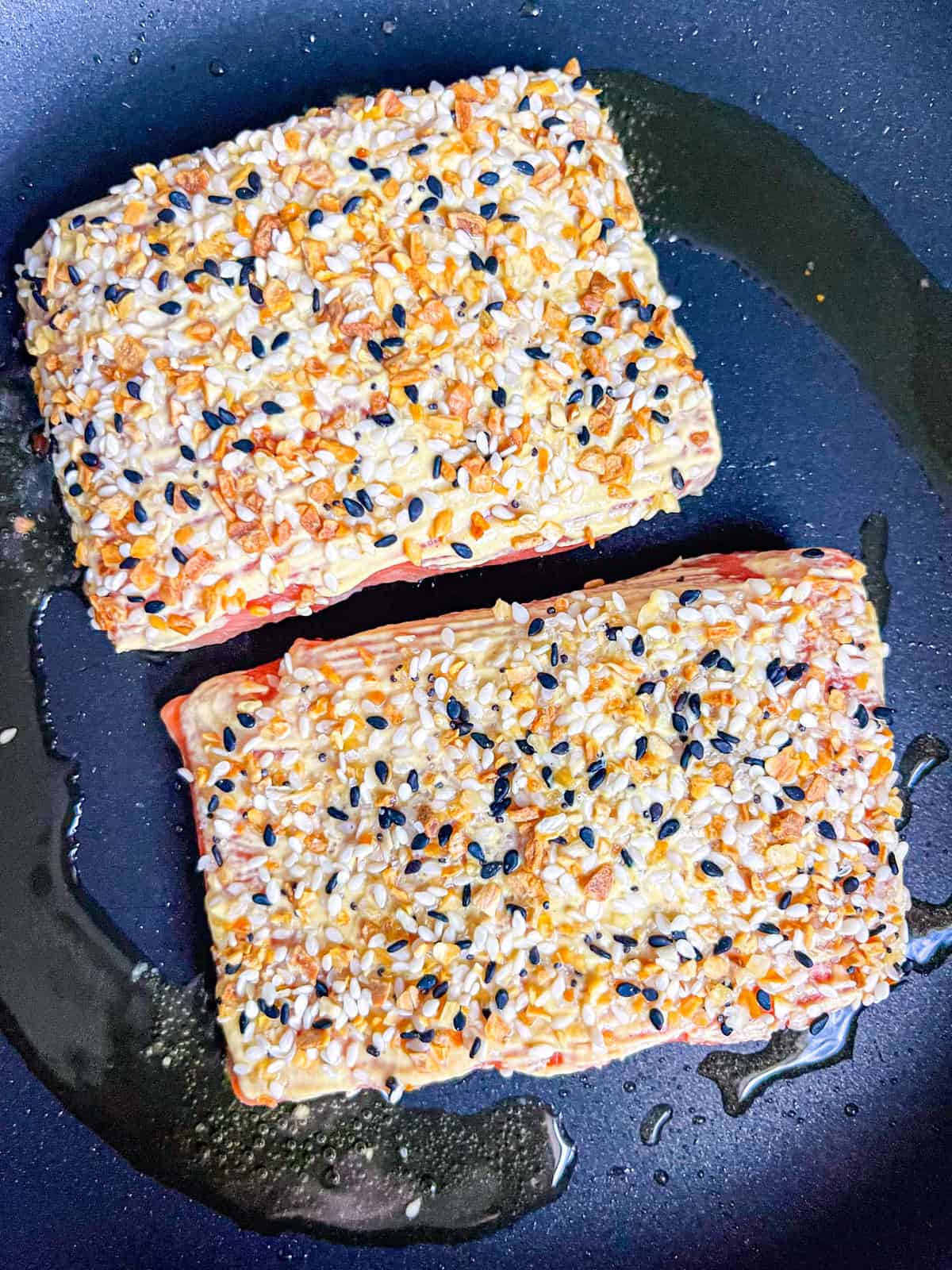 2 pieces of salmon with bagel seasoning cooking in a pan.