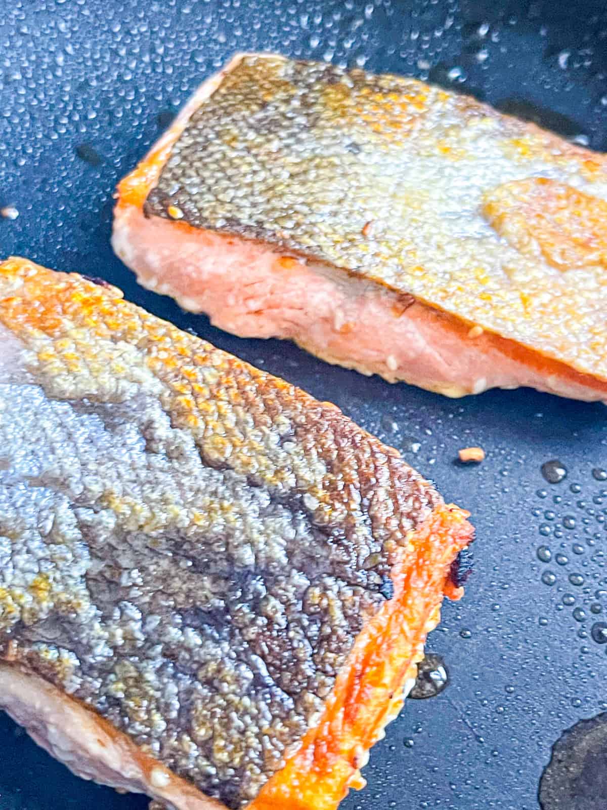 2 pieces of salmon cooking in a pan.