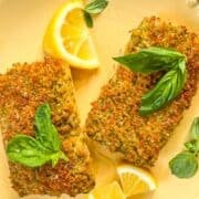 two golden brown Mahi Mahi fillets garnished with lemon wedges and fresh basil.