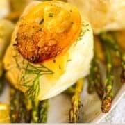 sea bass on a bed of asparagus on a white plate and garnished with lemons and dill.