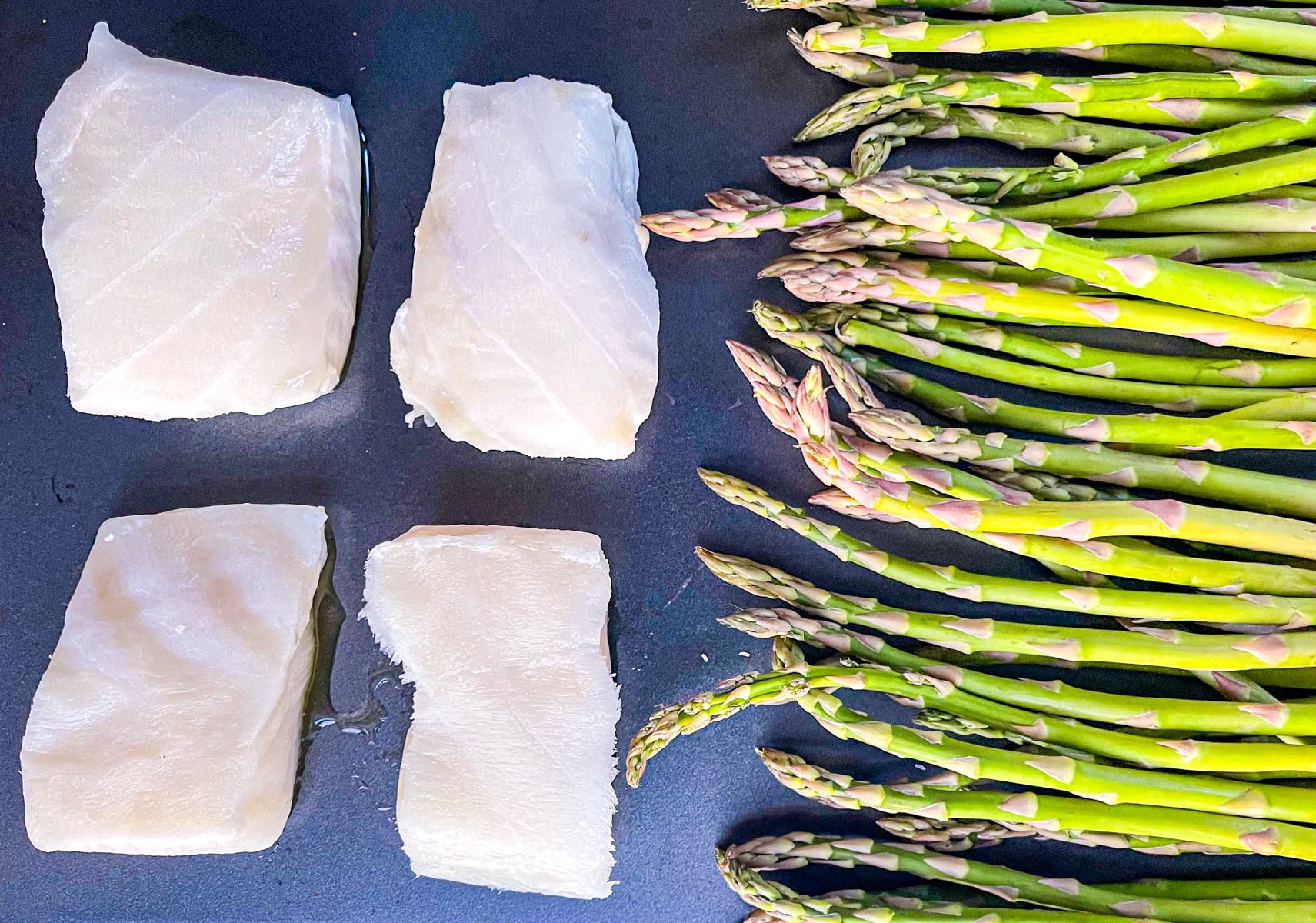 Asparagus on a baking tray with 4 pieces of Sea bass.