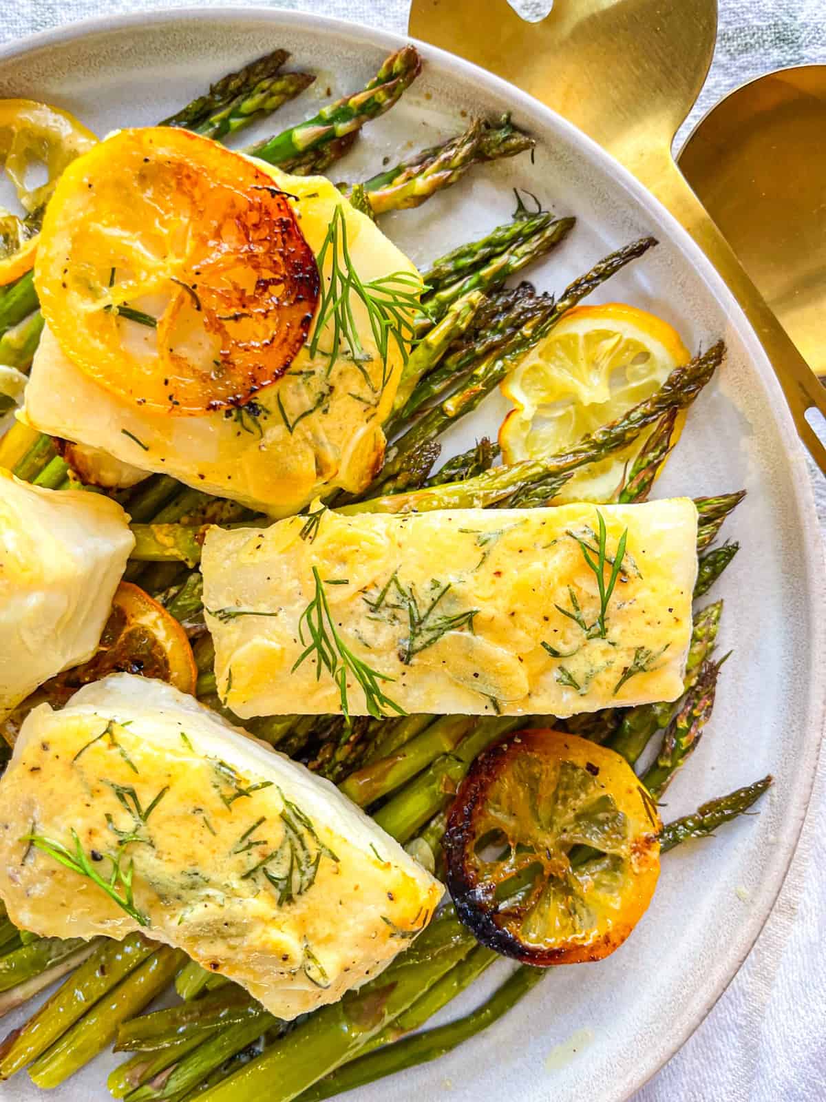4 chilean sea bass fillets on a bed of asparagus garnished with lemons and dill.