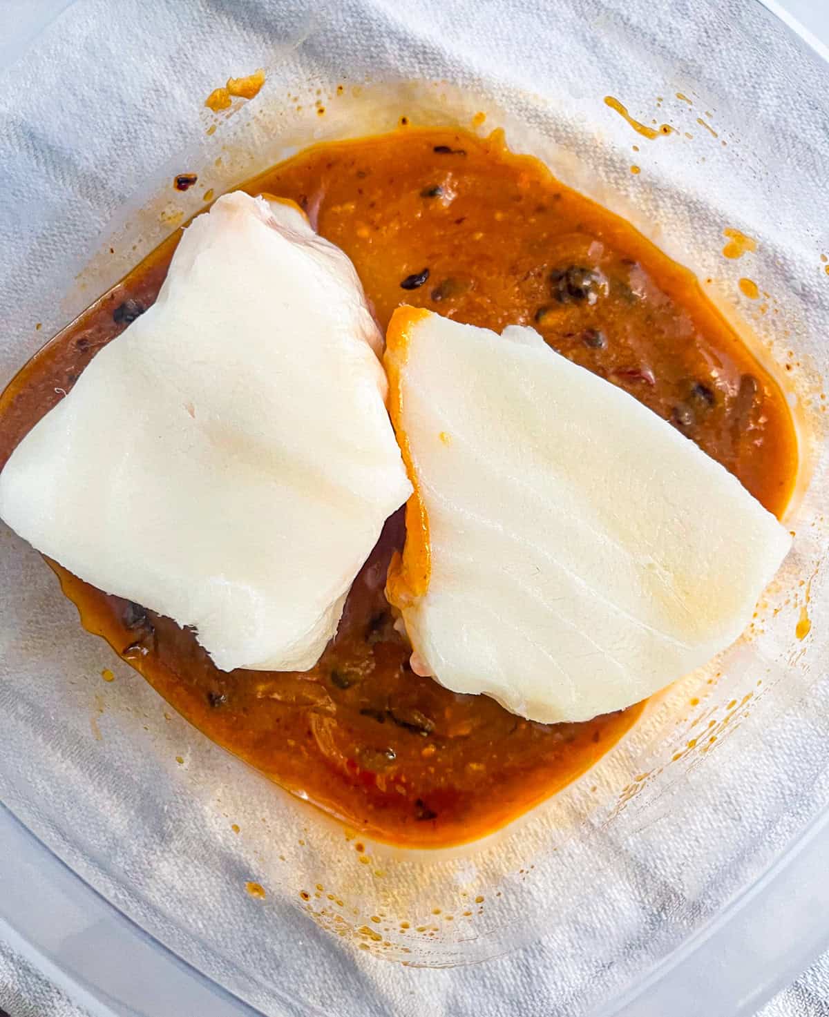 2 pieces of sea bass in a container with marinate.