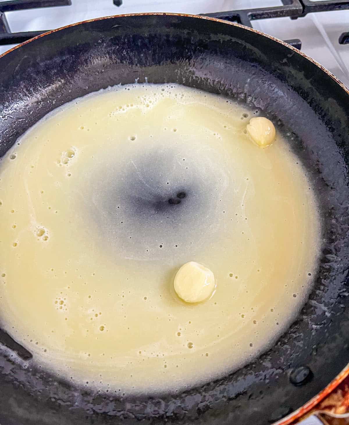 garlic cloves in butter sauce in a pan.