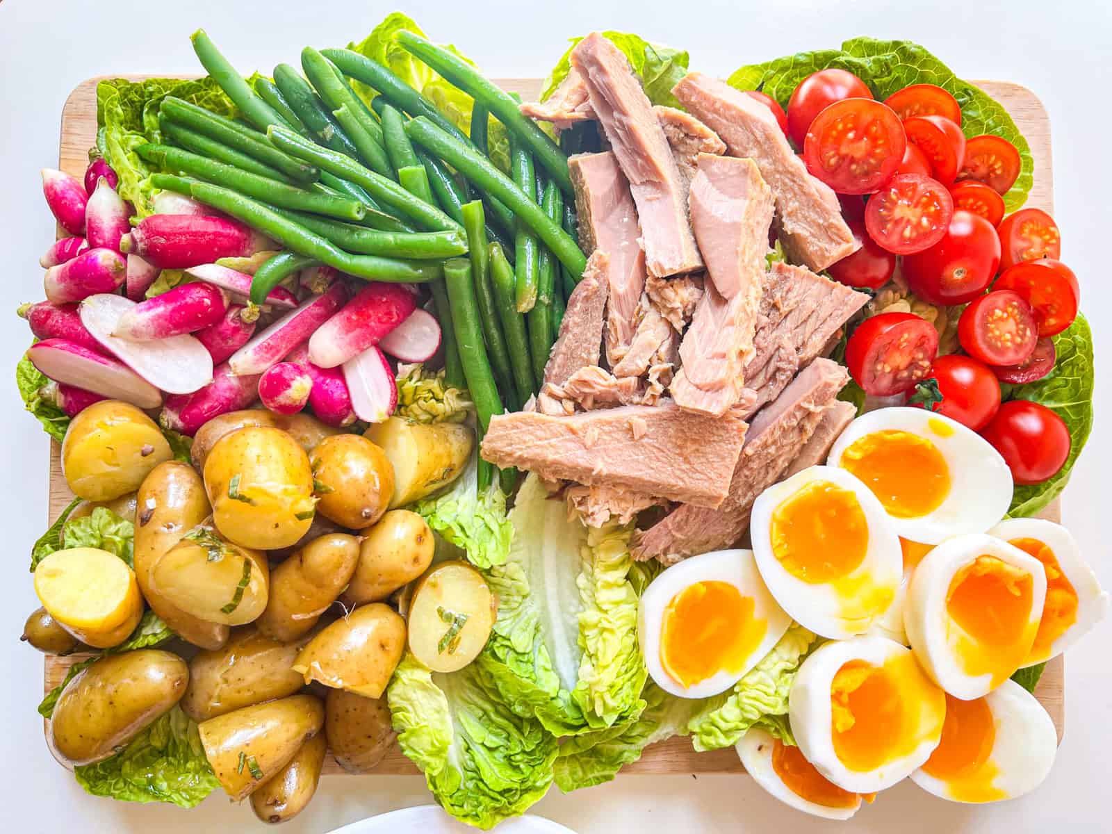 Nicoise Salad being assembled on a board.