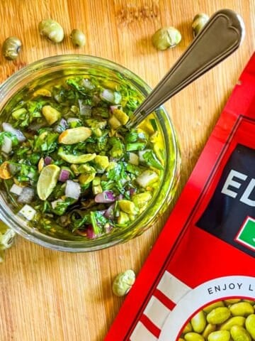 Bowl of chimichurri with edamame on a table next to a bag of edamame.