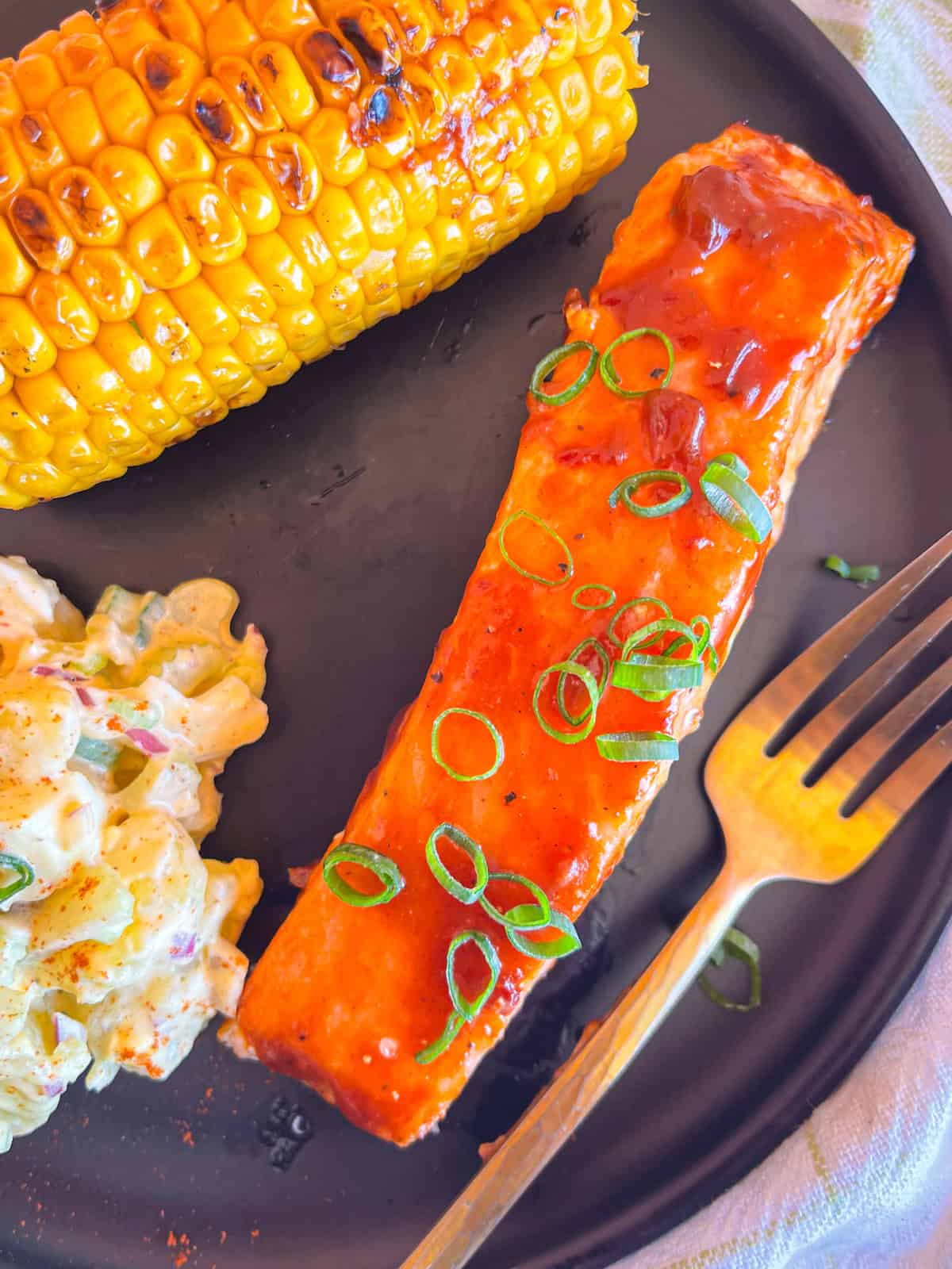 BBQ salmon fillet served with grilled corn and potato salad.