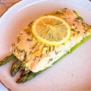 Salmon over asparagus on a white plate and garnished with a slice of lemon.