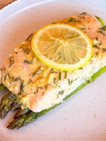 Salmon over asparagus on a white plate and garnished with a slice of lemon.
