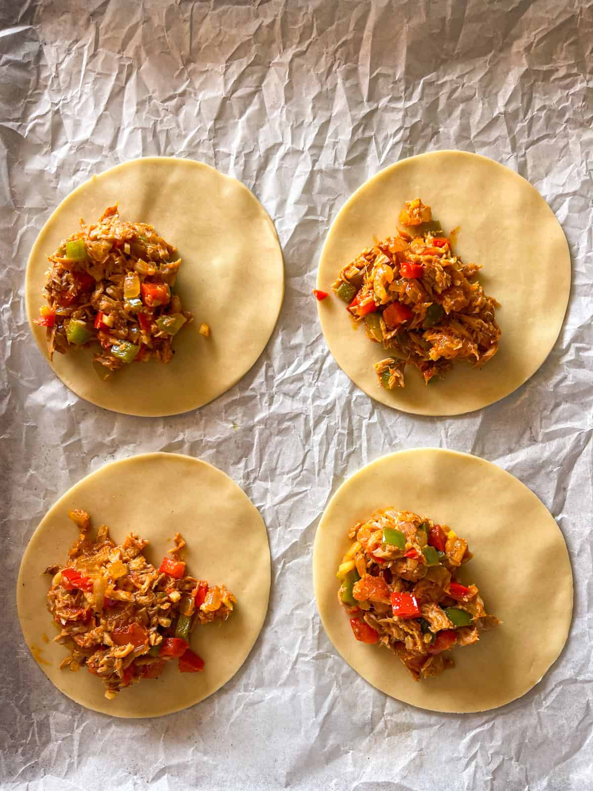 empanada wrappers filled with tuna veggie mix on baking sheet.