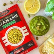Edamame Pesto on a table with basil, parmesan and lemon.
