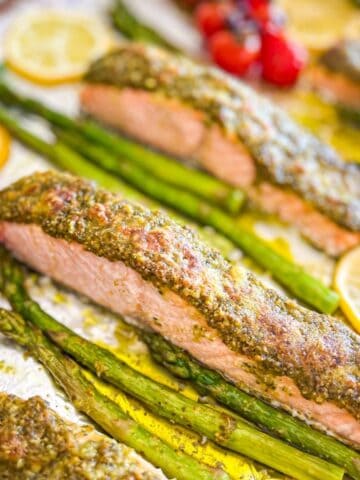 Pesto salmon on a tray with cherry tomatoes and asparagus.