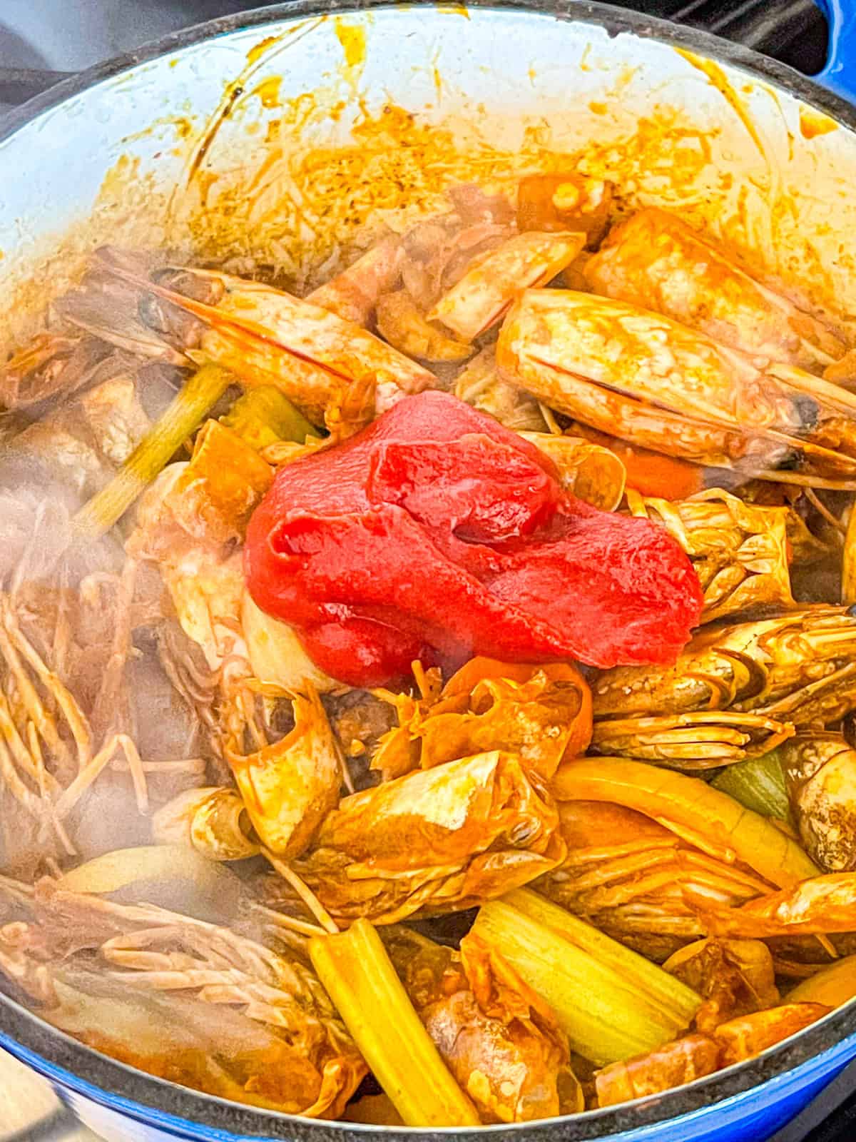 tomato paste added to shrimp shells in a pot.
