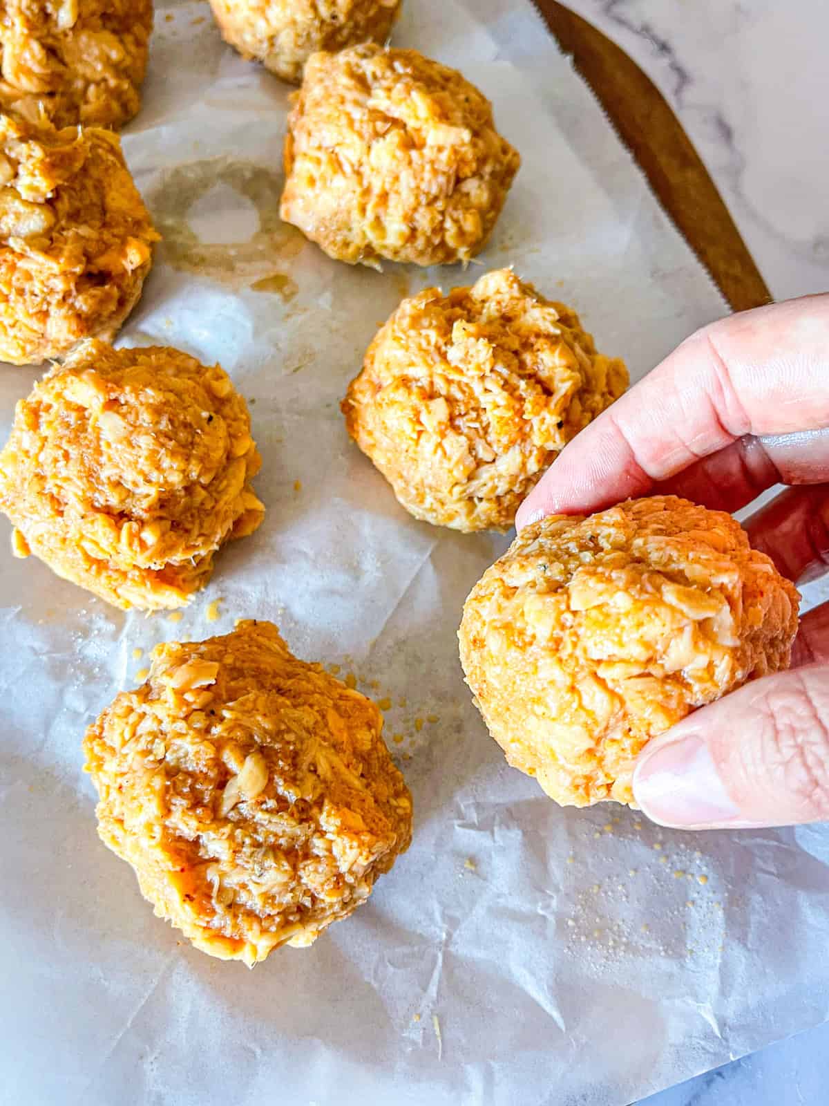 Salmon mixture in balls on a parchment paper lined sheet.