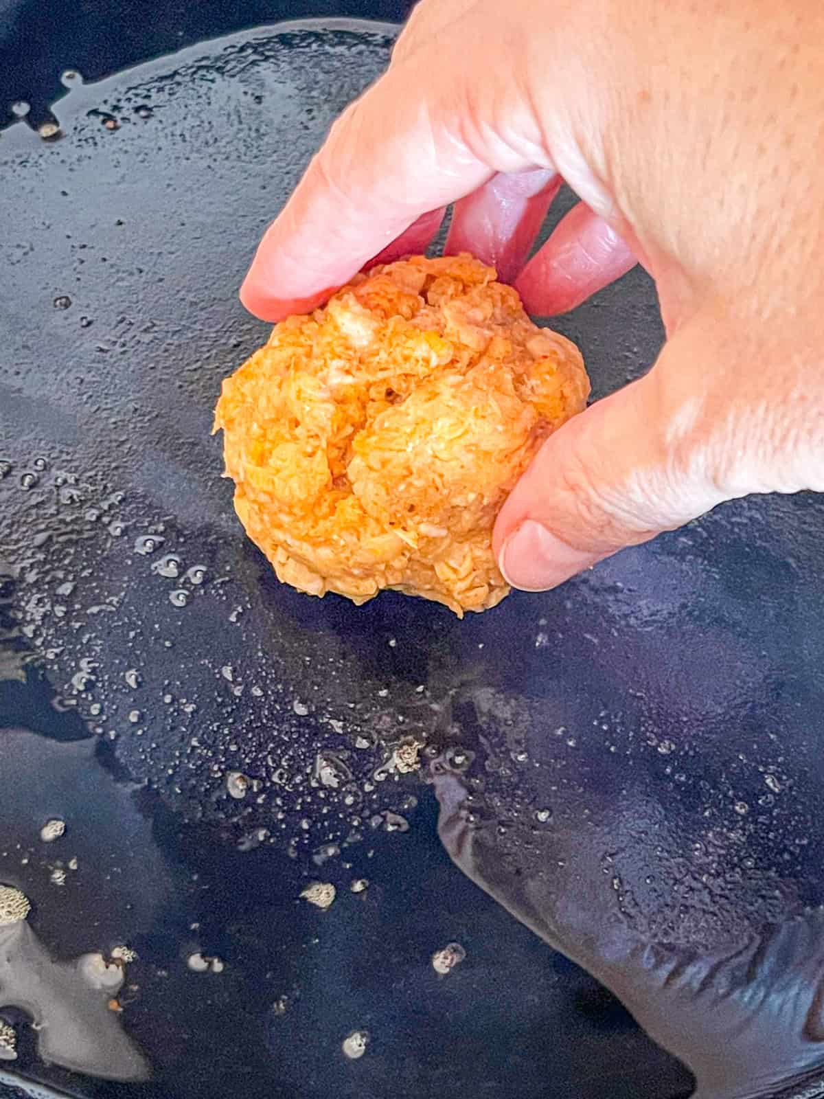Salmon burger ball being placed in a skillet.