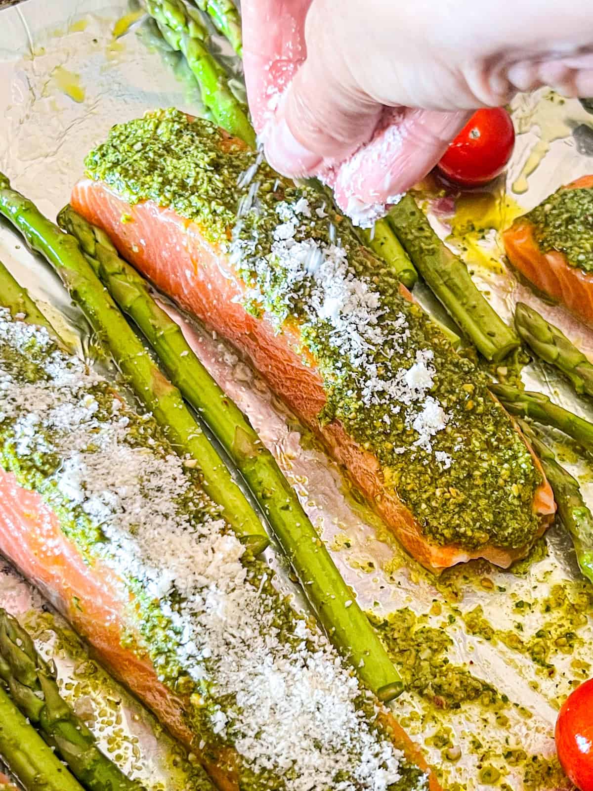 Sprinkling grated Parmesan over pesto-topped salmon fillets.