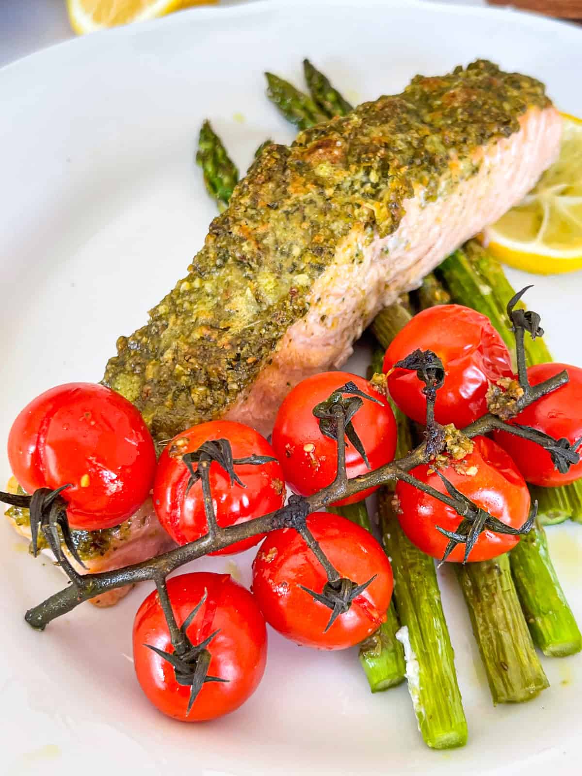 Pesto salmon on a plate with cherry tomatoes and asparagus.