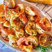 Platter of shrimp scampi without wine garnished with grilled lemon and diced parsley.