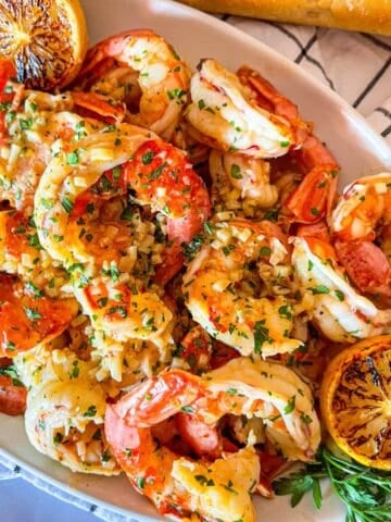 Platter of shrimp scampi without wine garnished with grilled lemon and diced parsley.