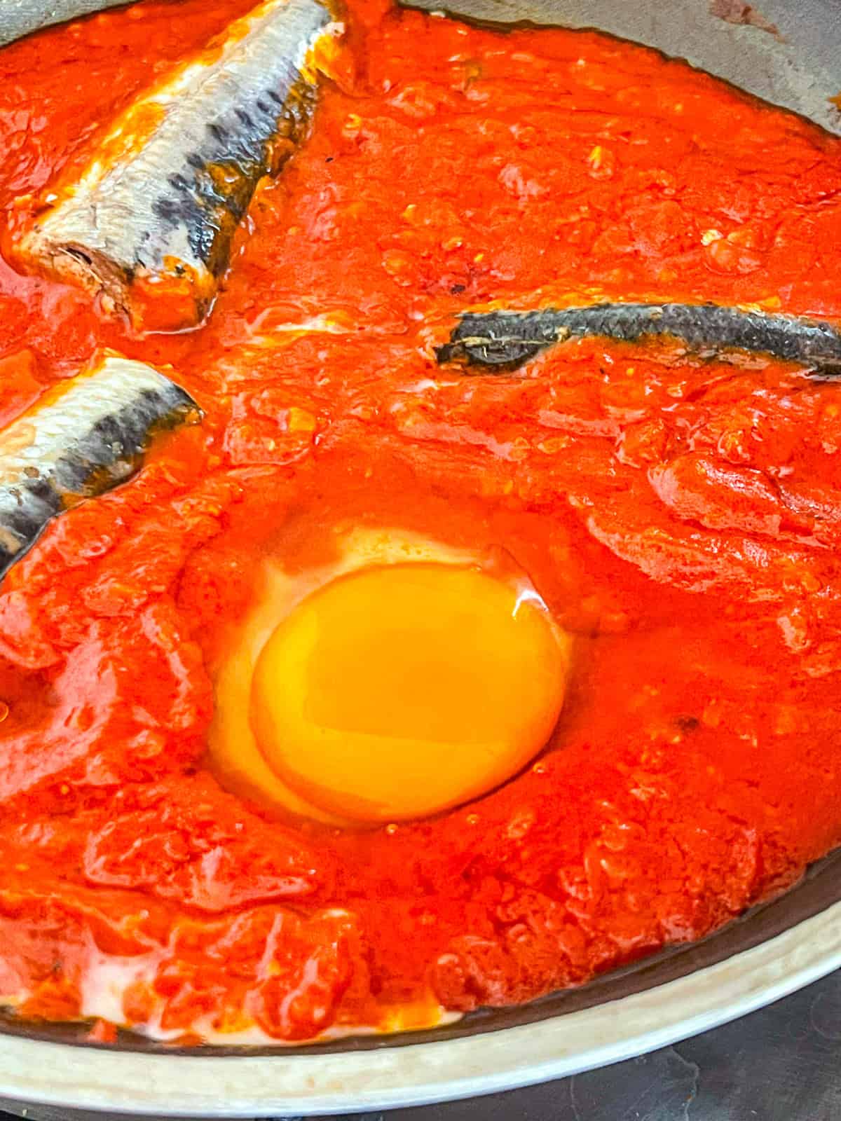Marinara sardines and egg cooked in a skillet.